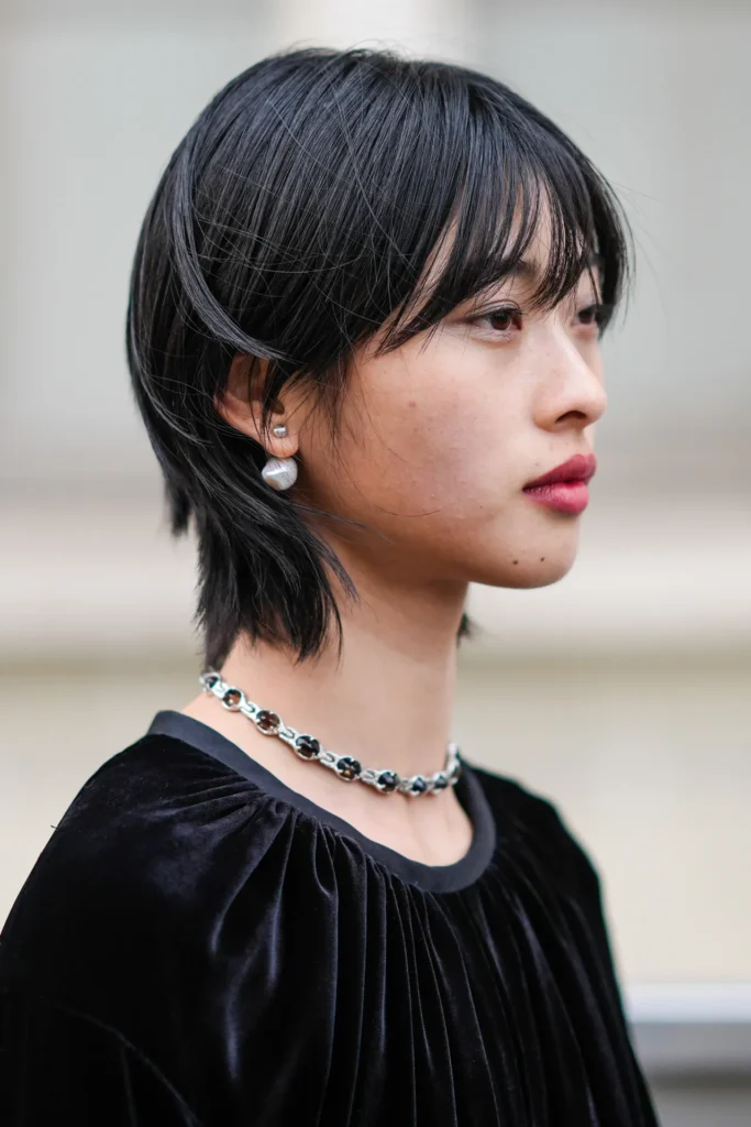 10 Stunning Pixie Haircuts for Black Women 2 A close-up profile of a person with sleek black hair, wearing pearl earrings and a silver floral-patterned necklace, dressed in a plush black top.
