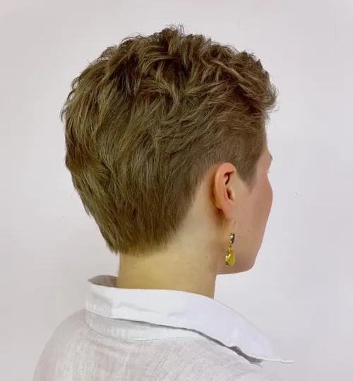 Short, textured hairstyle with curls, viewed from the back. The person wears a white shirt and a yellow earring.